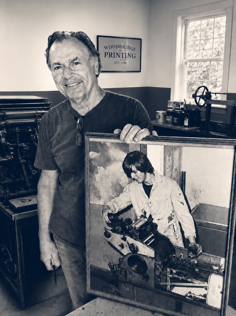 Frank Racz in the family print shop, holding a photo of himself at the press in the early days